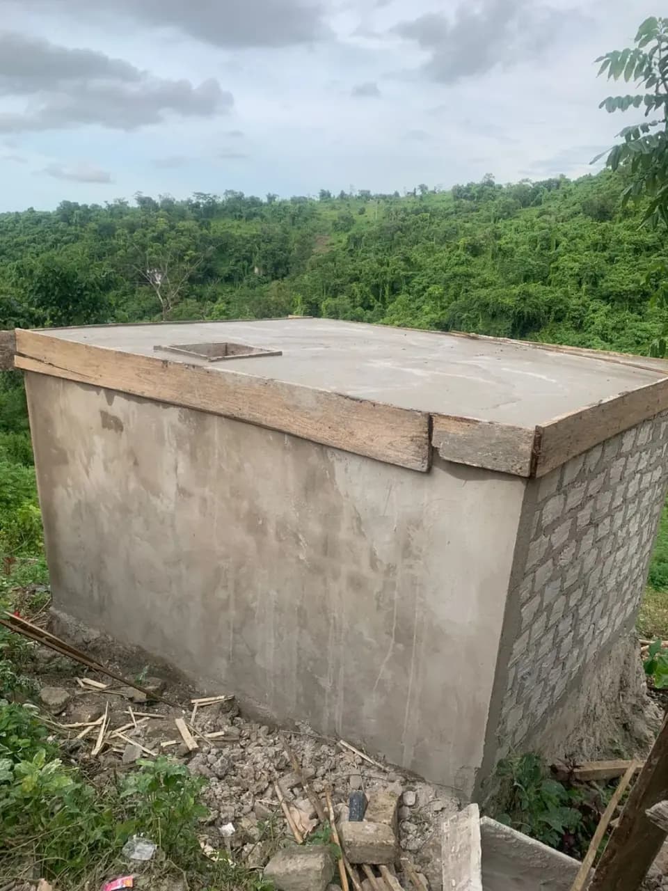 Tangki air hujan yang sudah selesai, sebuah bak beton persegi dengan tutup beton, di lereng bukit.