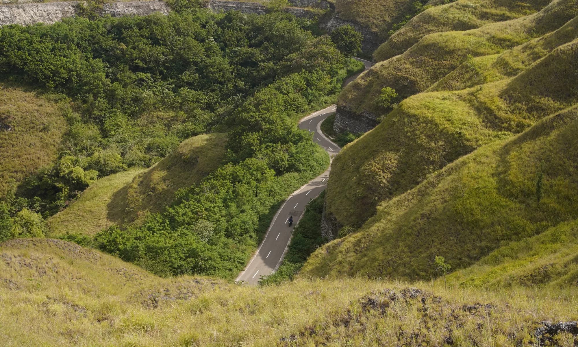 A sealed road switchbacking down through the Sumba highlands, with the valley beyond.