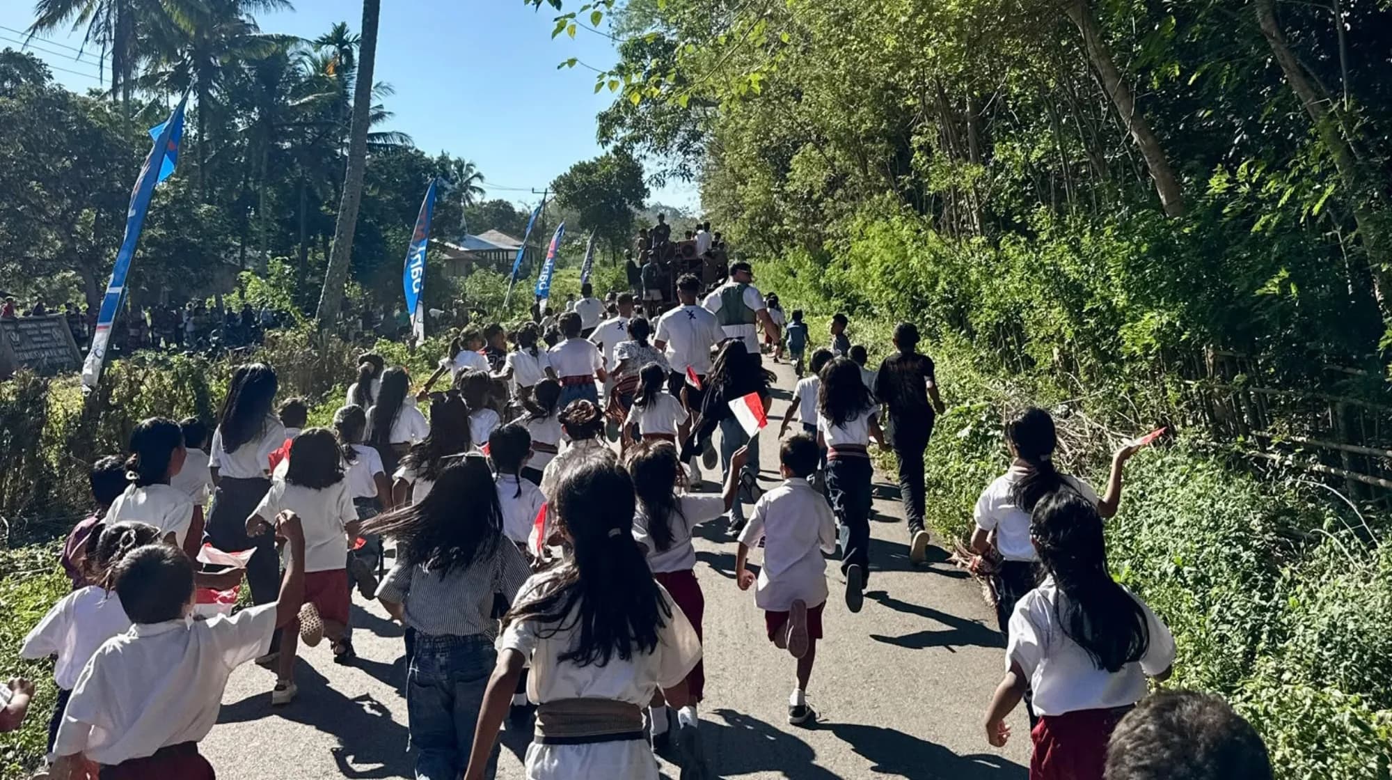 Schoolchildren in white and red uniform running away down a village road in Sumba.
