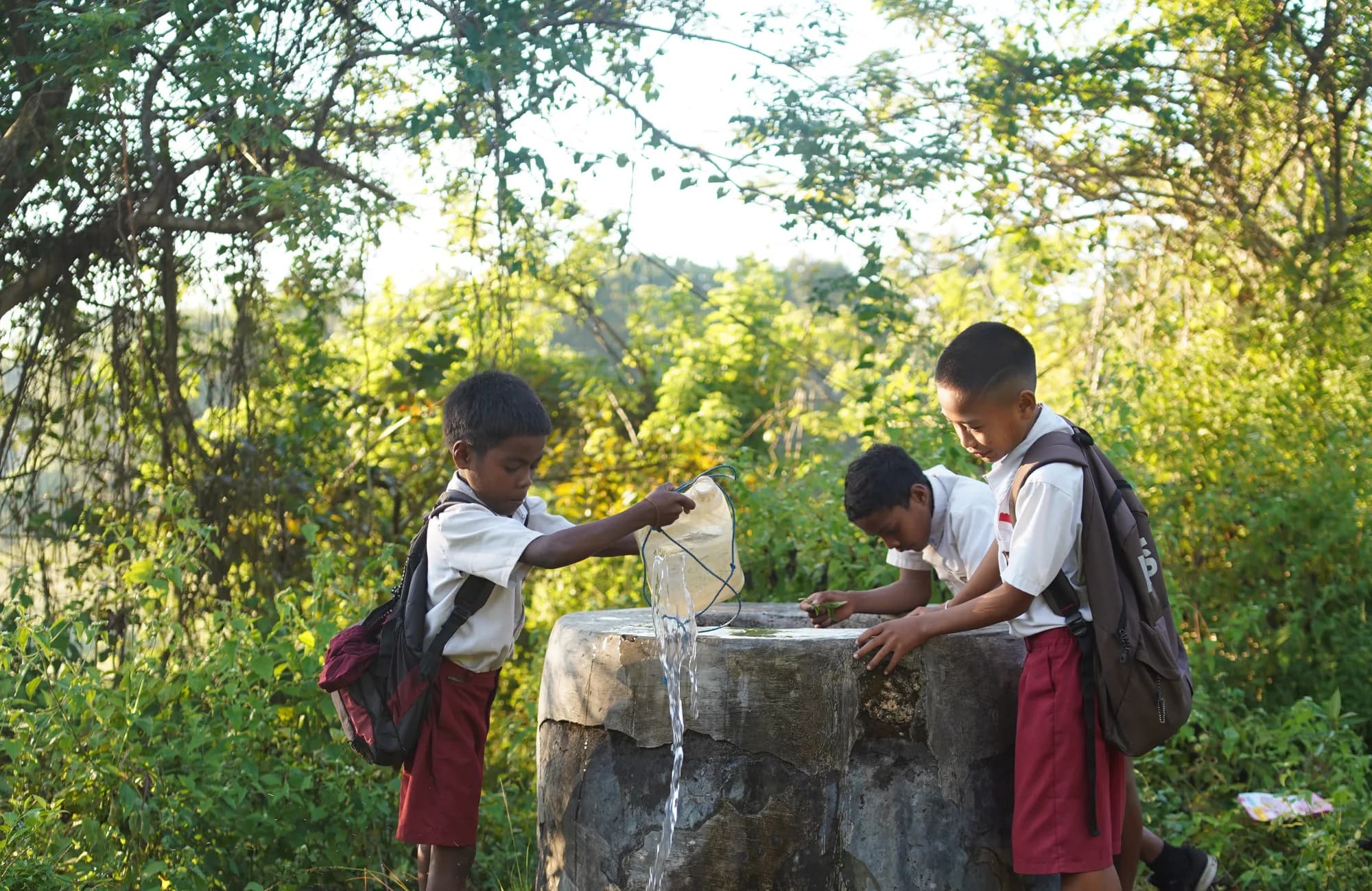 Tiga anak berseragam sekolah mengisi wadah air di sebuah bak batu di Sumba.